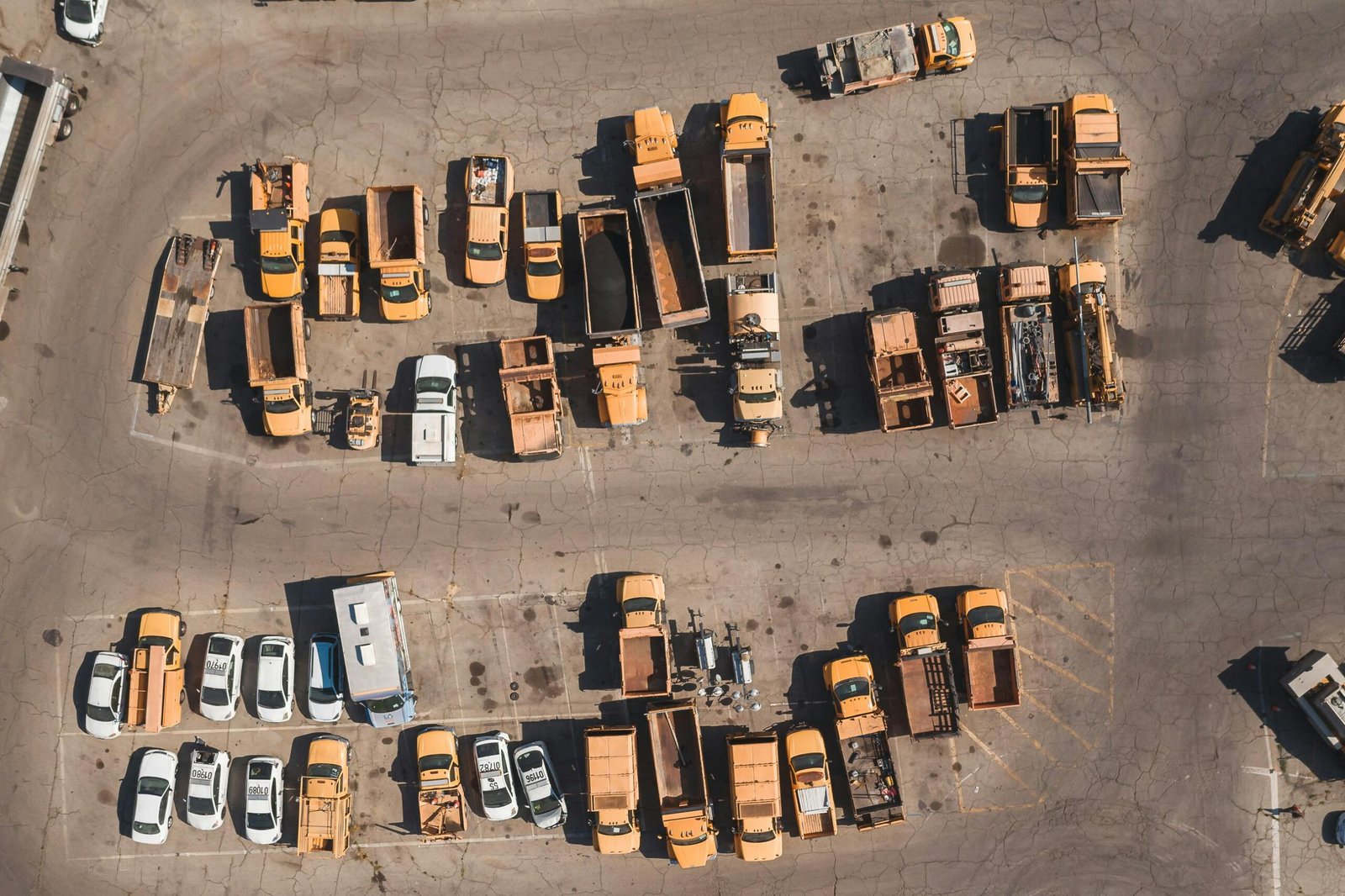Top-down aerial view of various parked utility and service vehicles in a large industrial parking lot.